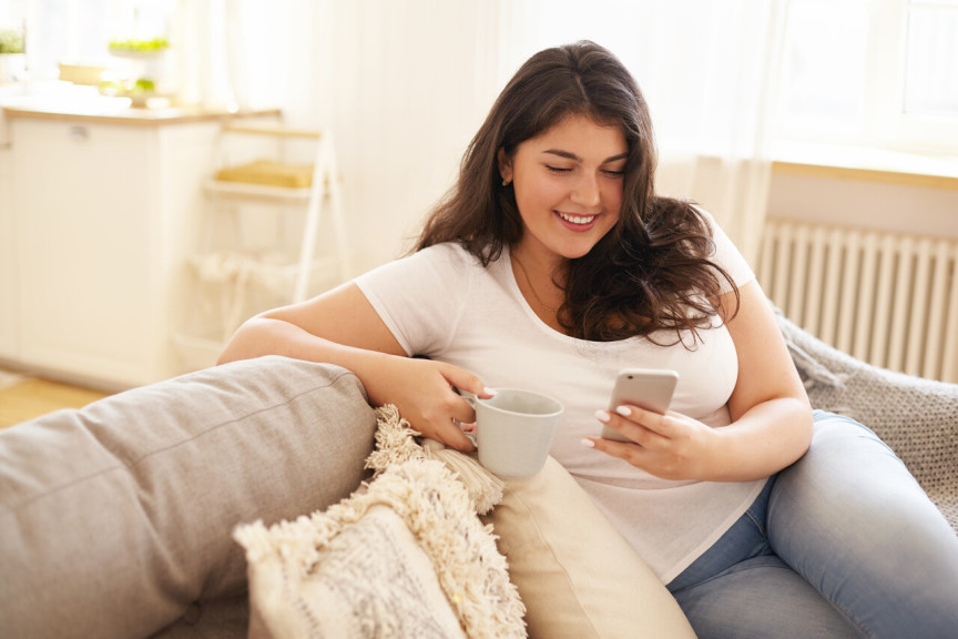 woman on couch with a coffee cup and mobile phone